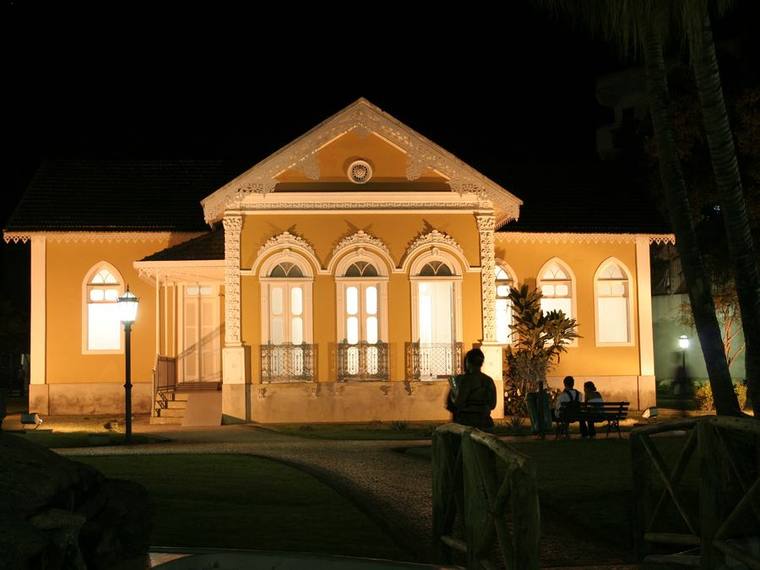 An ornate single-storey house with arched windows, lit warmly against the night.