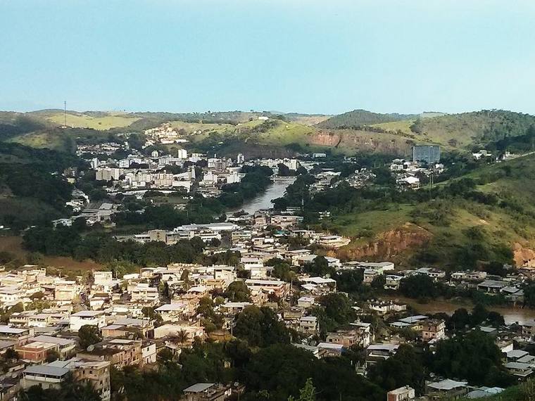 Cataguases seen from a hillside, houses spreading across the valley with the river winding through and green hills beyond.
